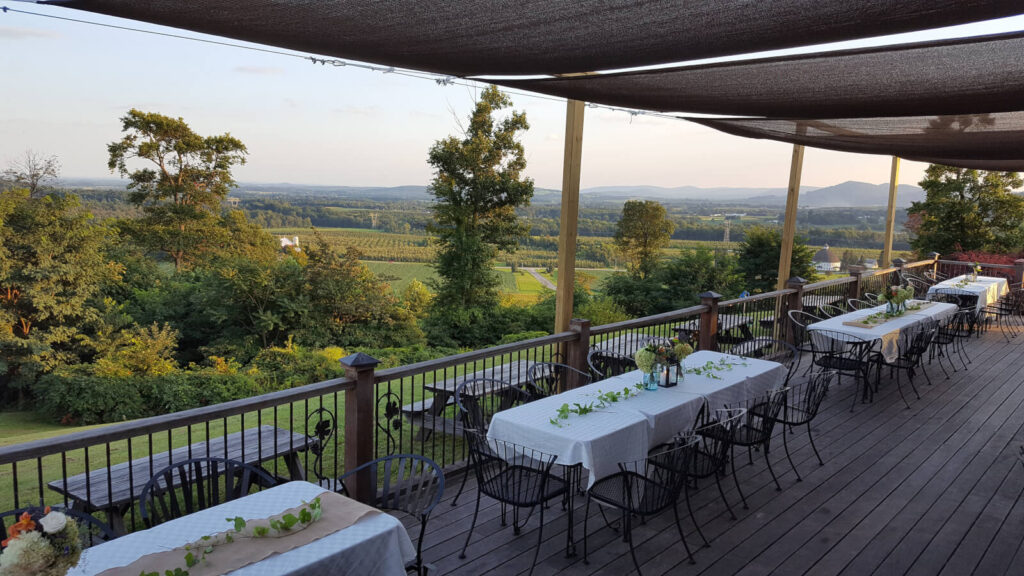 Outdoor dining area with long tables draped in white cloths and simple centerpieces, overlooking a scenic rural landscape with fields and distant hills—perfect for those seeking charming Gettysburg wedding venues.