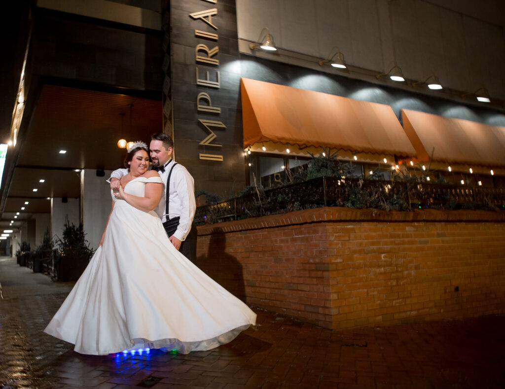A bride and groom embrace and dance outside a building marked "IMPERIAL" at night, the bride's dress flaring out as they stand on a brick sidewalk—one of the top wedding venues in Lancaster PA.